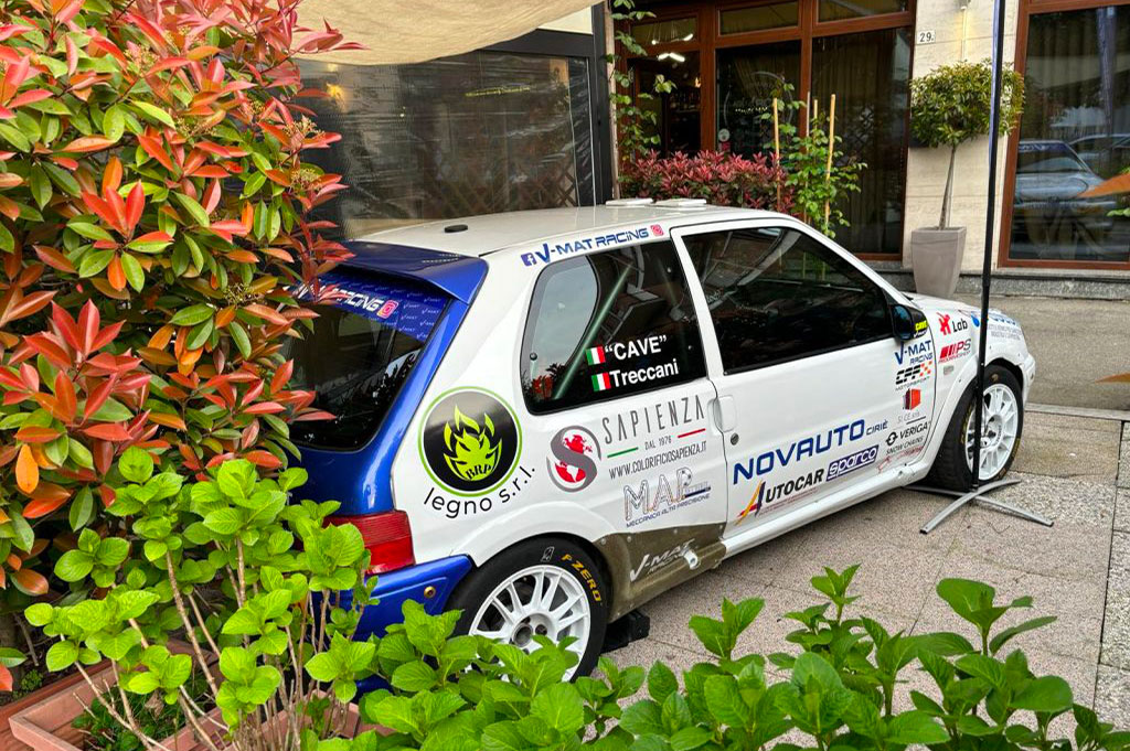 Auto da corsa parzialmente nascosta tra piante ornamentali, logo BRP Legno visibile